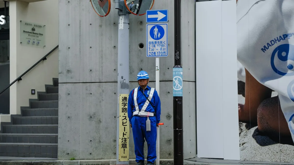 工事現場の前で交通誘導を行う青い制服の警備員
